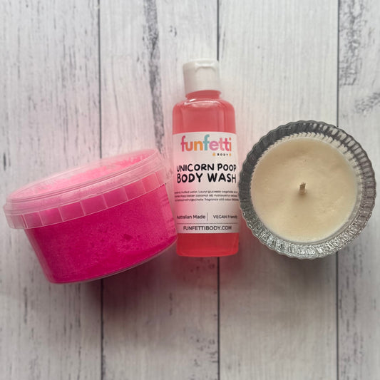 Pink container, bottle of 'funfetti' unicorn poop body wash, and candle on a wooden surface.
