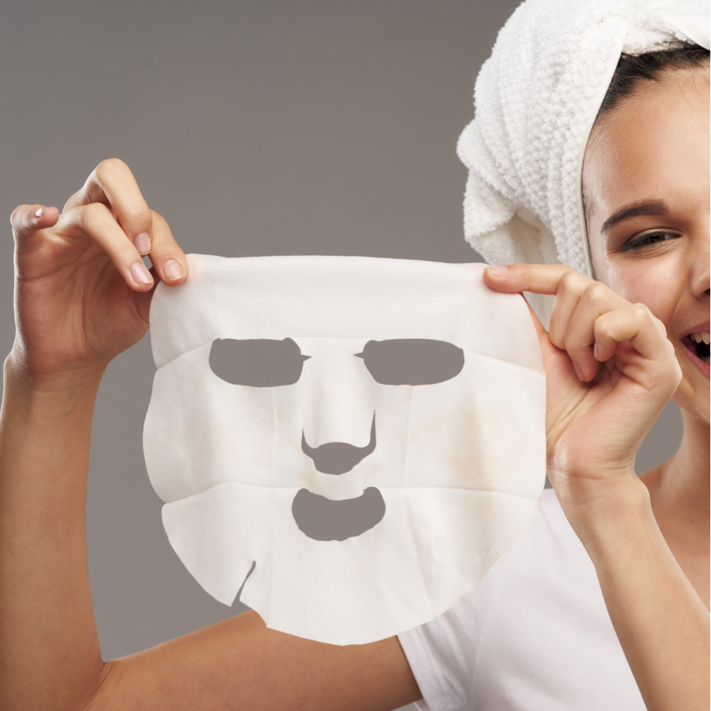Woman holding a white face mask against a gray background